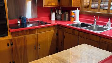 Una cocina con armarios de madera, encimera roja, pileta de acero inoxidable y ventana con contraventanas.