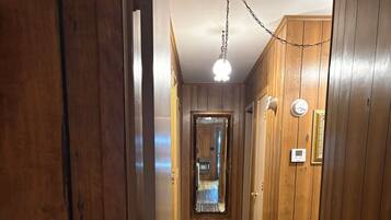 Un pasillo de madera con un tapete estampado, un espejo y un termostato en la pared.