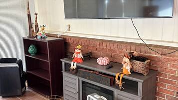 Een woonkamer met een flatscreen televisie aan de muur, een open haard, een boekenplank en een vloerkleed met een patroon.