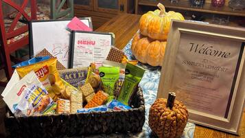 Un cartel de bienvenida, una cesta de aperitivos y una calabaza sobre una mesa en una habitación acogedora con muebles de madera y un mantel estampado.