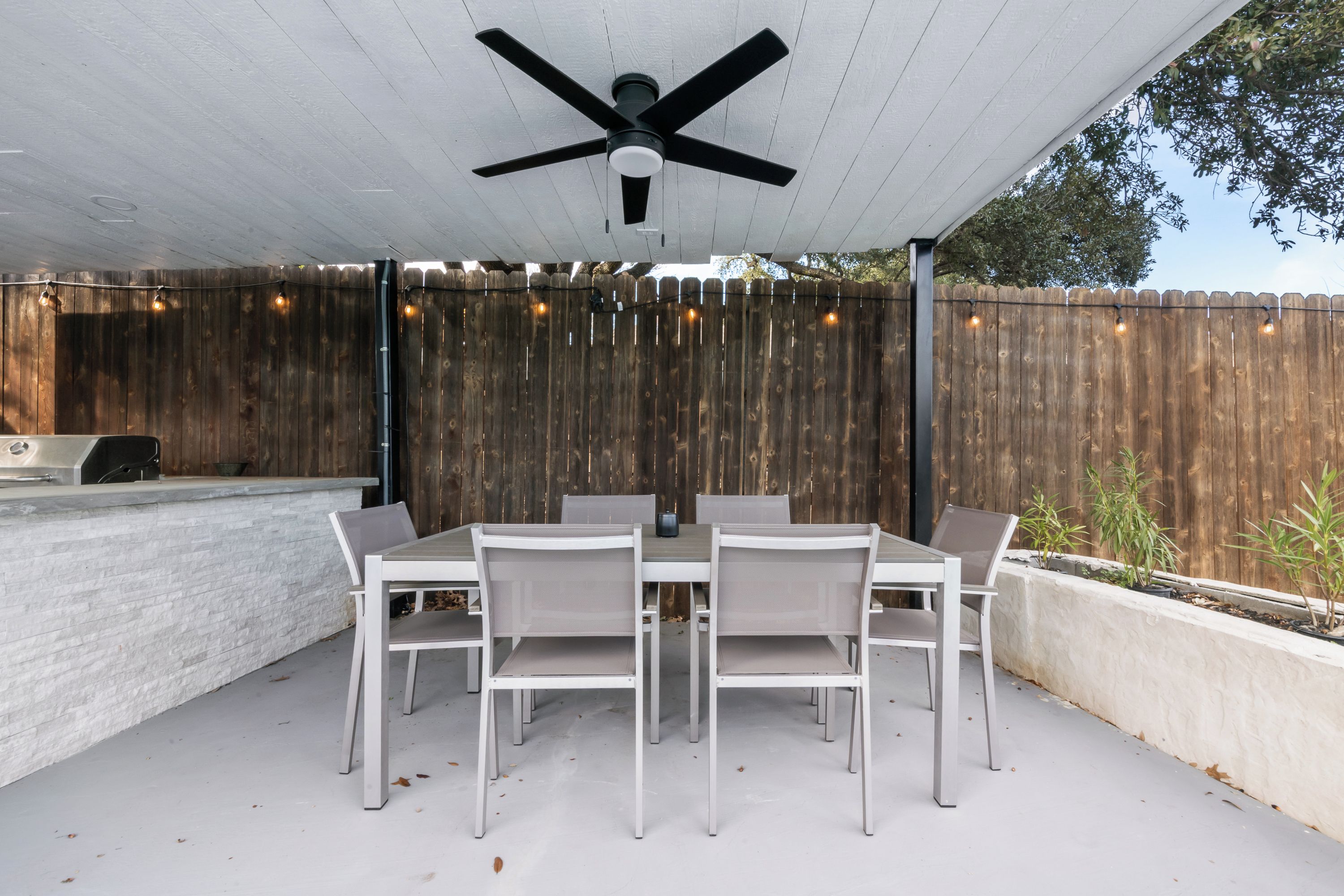 An outdoor patio with a table and chairs, a ceiling fan, and a wooden fence.