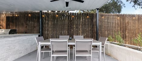 An outdoor patio with a table and chairs, a ceiling fan, and a wooden fence.