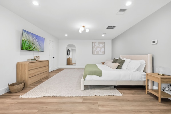 Ein modernes Schlafzimmer mit Bett, Nachttisch, Kommode und Kunstwerk an der Wand.
