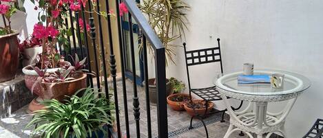 Una terraza con plantas en macetas, una escalera, una mesa redonda con sillas y un farol fijado a la pared.