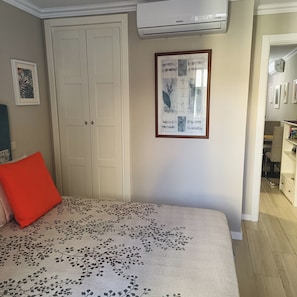 A bedroom with a bed, a red pillow, a wall-mounted air conditioner, a framed artwork, and a door. - A Little Gem centrally located in Quaint Olhão, East Algarve (Olhão)