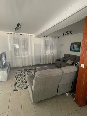 A living room with a grey sofa, a television, and a patterned rug. - Maison 3 chambres avec patio centre ville de Jonzac animaux acceptés (Jonzac)