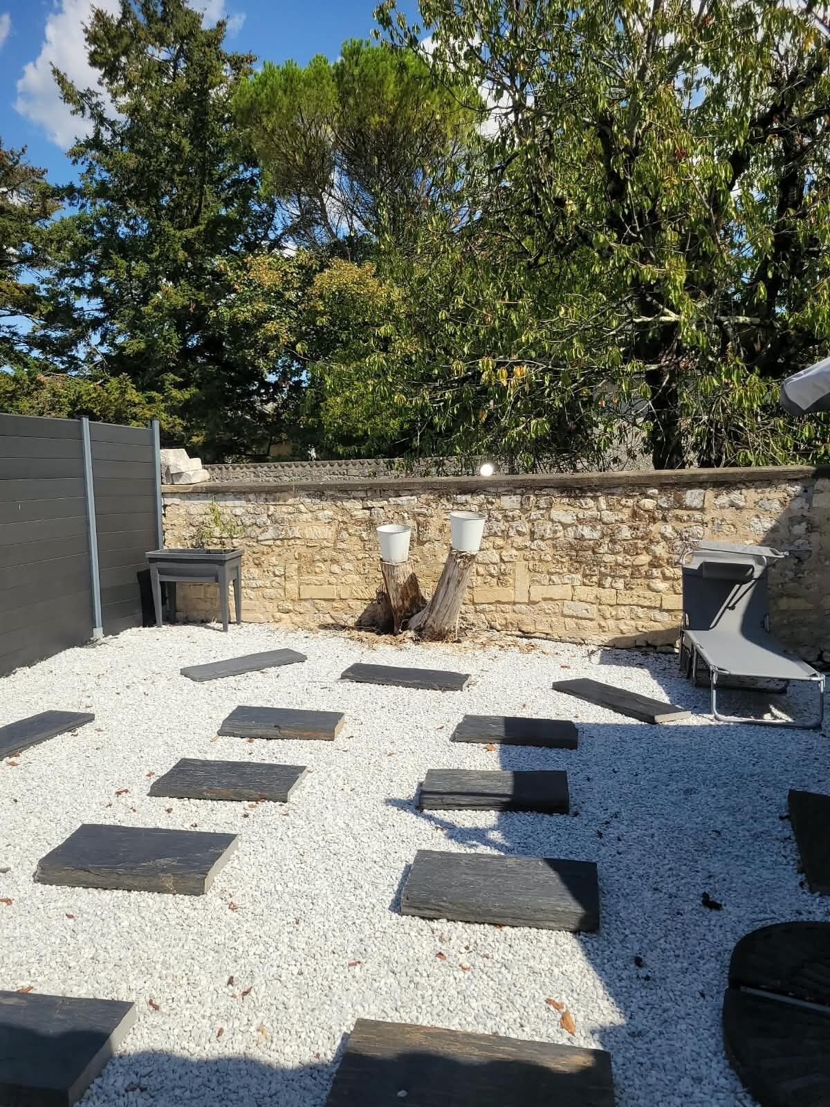 Un espace extérieur aménagé avec des murs en pierre, un sol de gravier et des arbres en arrière-plan.