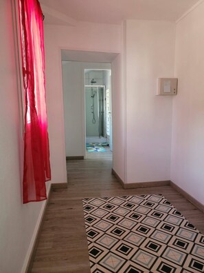 A hallway with a patterned floor, a red curtain, and a shower area in the distance. - Maison 3 chambres avec patio centre ville de Jonzac animaux acceptés (Jonzac)