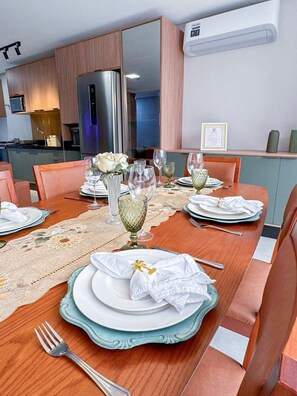 A dining area with a wooden table set for four, a refrigerator in the background, and a framed certificate on the wall. - Atlantic Residence Carneiros (Tamandaré)