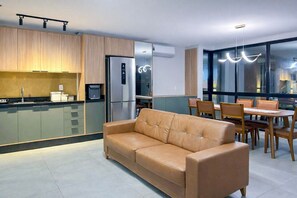 A modern kitchen with a built-in refrigerator, a dining area with a table and chairs, and a leather sofa. - Atlantic Residence Carneiros (Tamandaré)