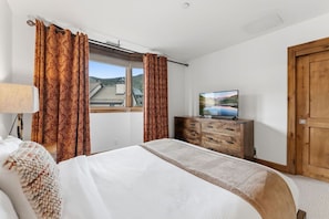 Ein Schlafzimmer mit einem Bett, einem Schminktisch, einem Fernseher und einem Fenster mit Vorhängen.