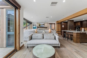 Ein modernes Wohnzimmer mit einem grauen Sofa, einem runden Hocker und einer Küchenzeile mit Holdekor.