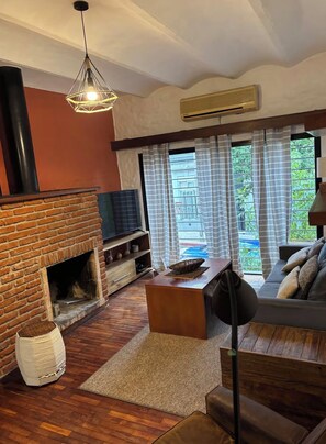 A living room with a brick fireplace, a sofa, a television, and a large window with curtains. - Modern & Spacious Duplex in Montevideo | 3 Bedrooms, 2 Bathrooms, and Wi-Fi (Montevideo)