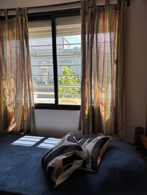 Une chambre avec un lit, une fenêtre avec des rideaux et une vue sur un bâtiment à l’extérieur.