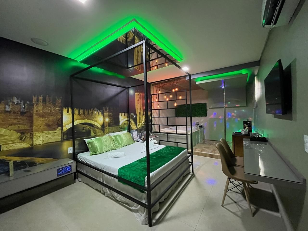 Una cama con dosel con colcha verde, un escritorio con una silla y un televisor montado en la pared.