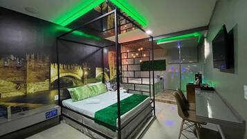 Una cama con dosel con colcha verde, un escritorio con una silla y un televisor montado en la pared.