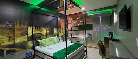 Una cama con dosel con colcha verde, un escritorio con una silla y un televisor montado en la pared.