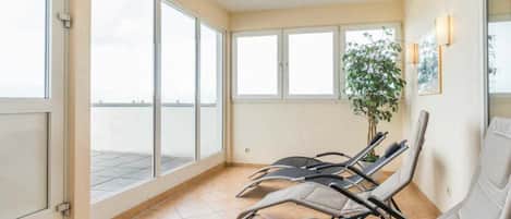 A waiting area with a view of the sea, a potted plant, and several reclining chairs.