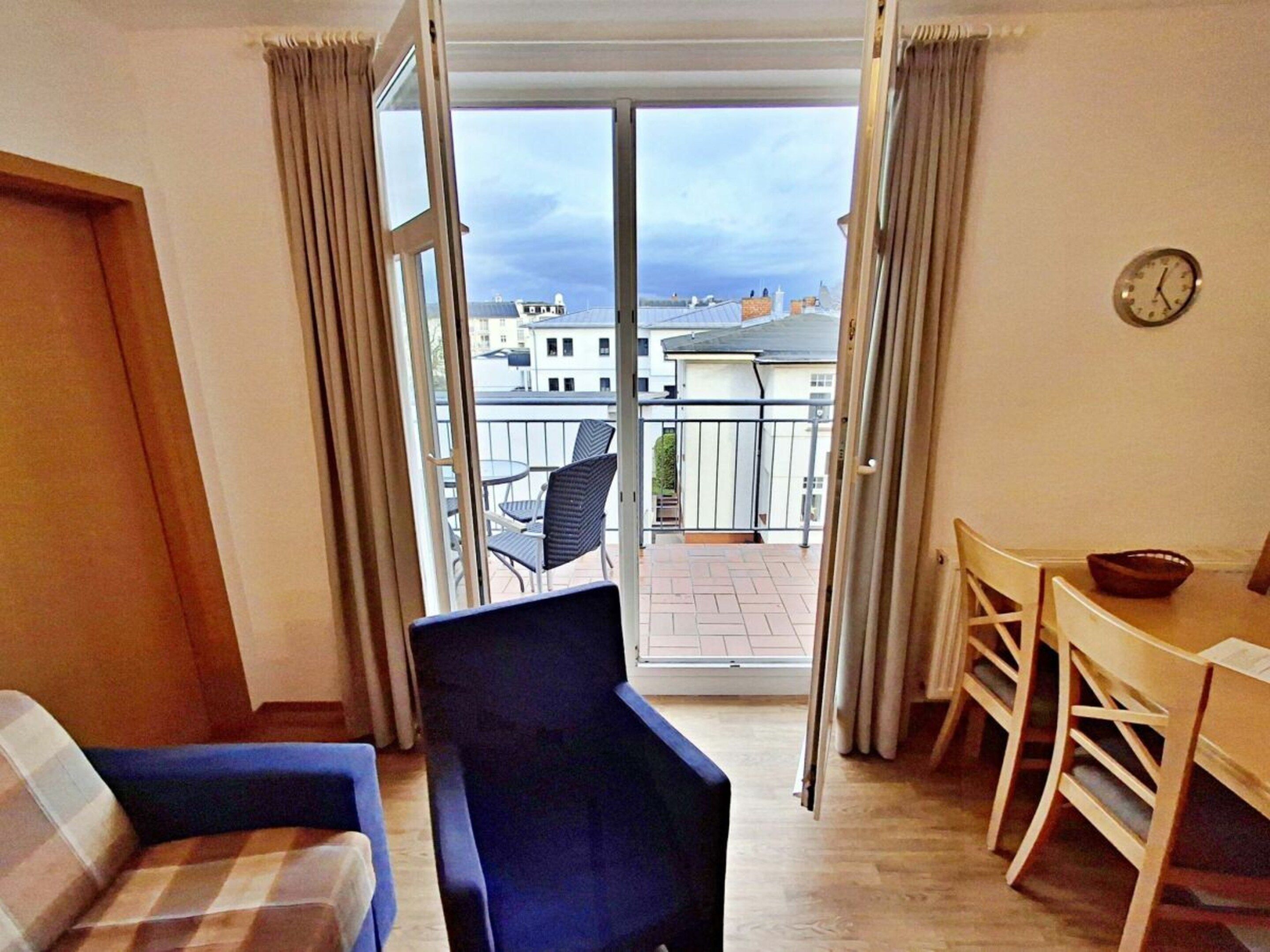 A room with a sofa, a chair, a dining table with chairs, and a view of buildings through a glass door.