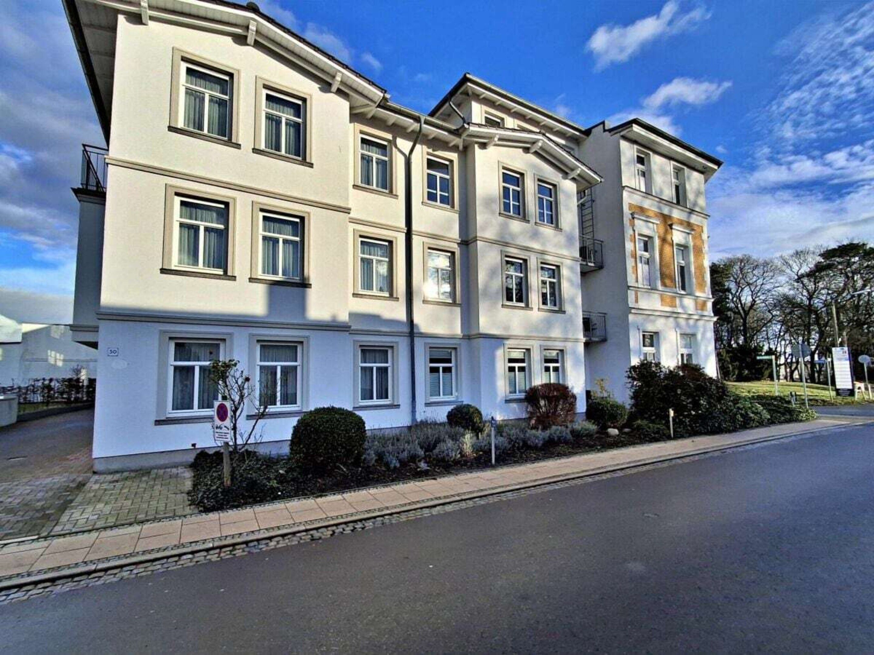 A multi-story residential building with a flat facade, multiple windows, and a paved driveway.