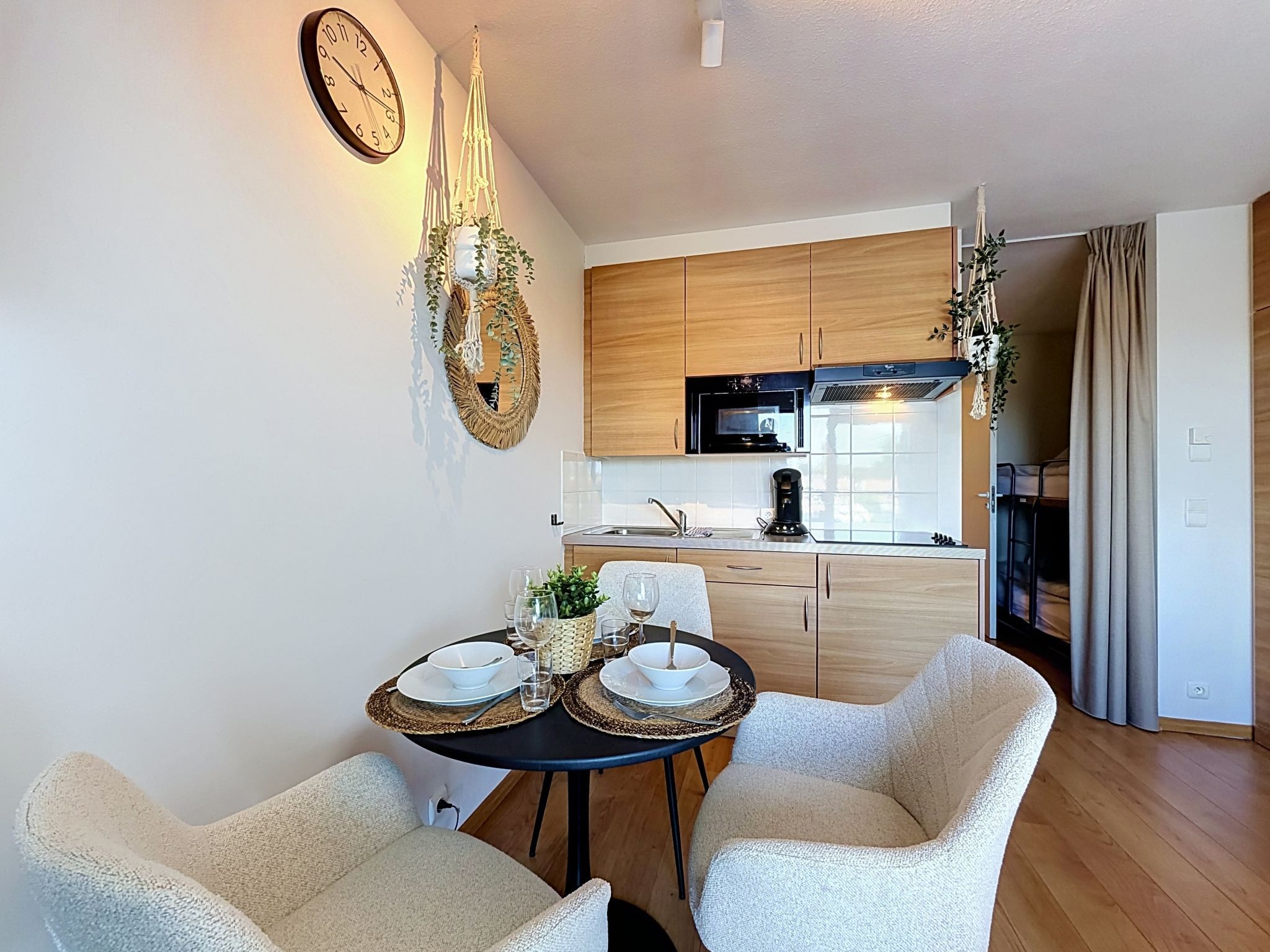 A modern kitchen with wooden cabinets, a black oven, and a dining area with two chairs and a table set for two.
