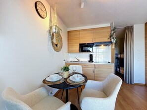 A modern kitchen with wooden cabinets, a black oven, and a dining area with two chairs and a table set for two. - Sea You @ Blutsyde by Interhome (Bredene)