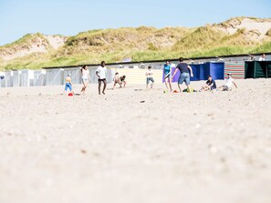 Ein Strand mit spielenden Personen und einer Reihe Strandkörben im Hintergrund.