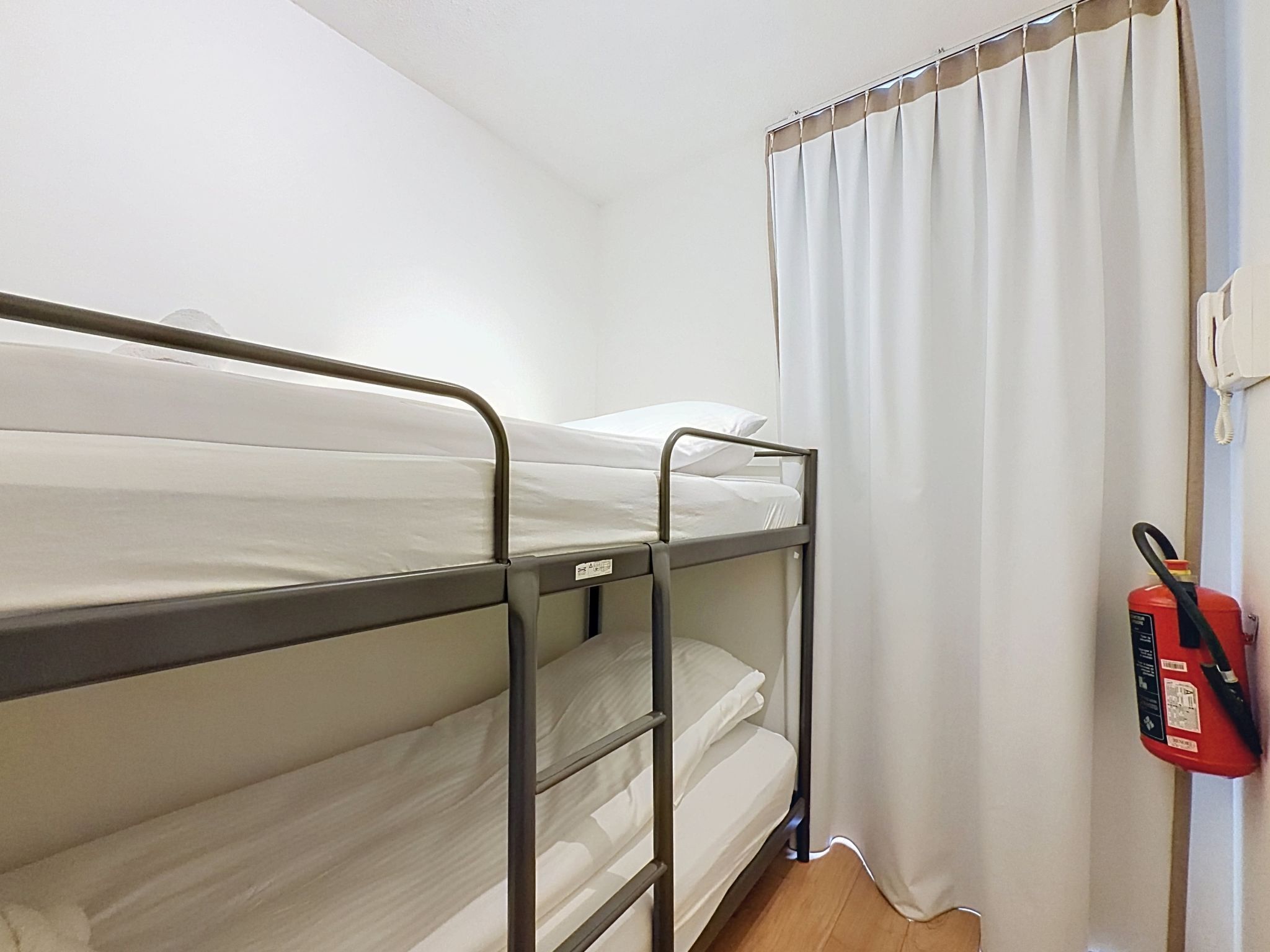 A bunk bed in a room with a curtain and a fire extinguisher on the wall.