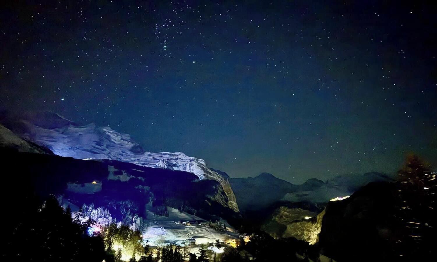 A night view of a mountainous area with snow-covered peaks and a starry sky.