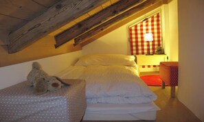 A bedroom with a sloped ceiling, a bed with white bedding, a teddy bear on a polka-dotted pillow, a red and white checkered curtain, and a small table with a lamp. - CHARMING CHALET RETREAT WITH SUNNY SOUTH-FACING TERRACE (Lauterbrunnen)