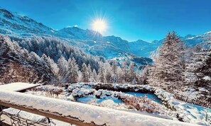 Paisagem montanhosa com piscina coberta de neve e árvores ao redor.