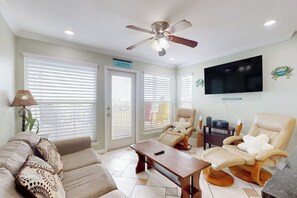 A living room with a sofa, armchairs, a coffee table, a ceiling fan, a TV, and a sign indicating a smoking area. - Seascape Condos - A SeaScape Paradise #1101 (Galveston)