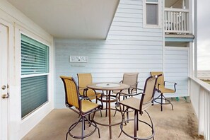A covered outdoor patio with a round table and six chairs, a sign reading 'FEELING NAUTI', and a white railing. - Seascape Condos - A SeaScape Paradise #1101 (Galveston)