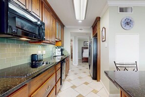A kitchen with wooden cabinets, a microwave, a refrigerator, and a dining table. - Seascape Condos - A SeaScape Paradise #1101 (Galveston)