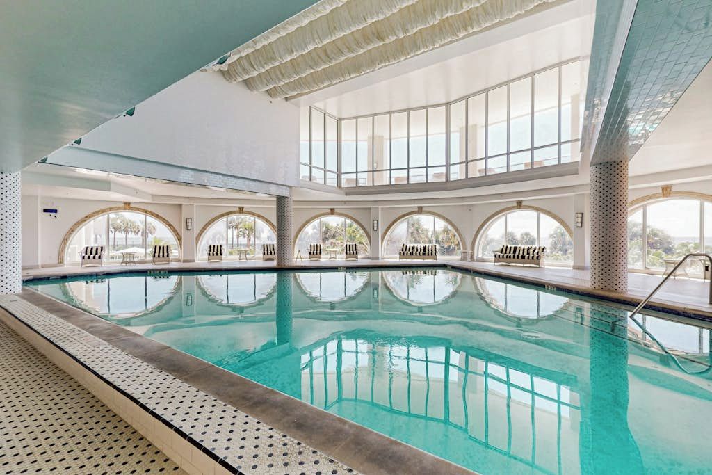 An indoor swimming pool with clear water, multiple levels of seating, and large windows.