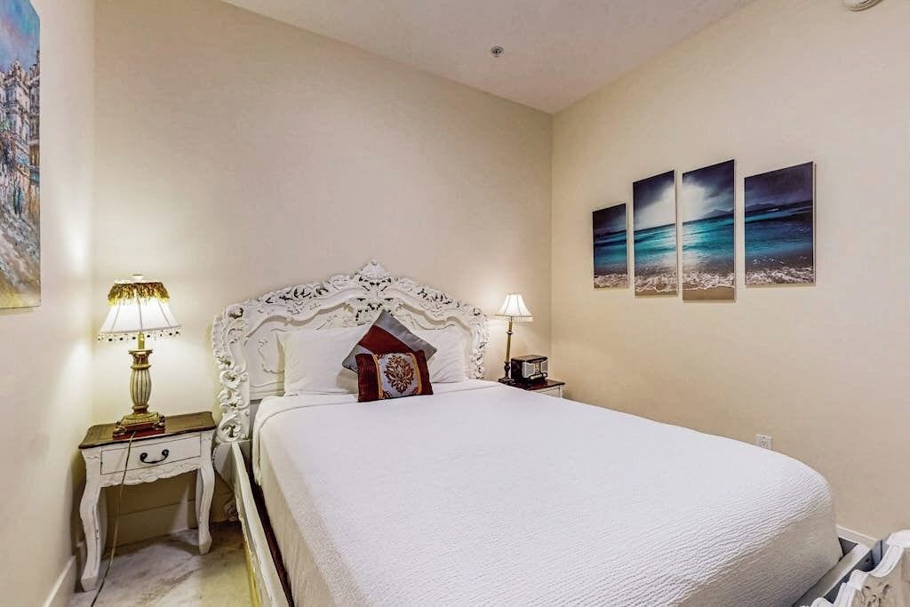 A bedroom with a large bed, two bedside tables, and three wall-mounted paintings.