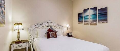A bedroom with a large bed, two bedside tables, and three wall-mounted paintings.