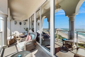 A balcony with wicker furniture, a glass door, and a view of the ocean. - Diamond Beach Resort Penthouse (Galveston)