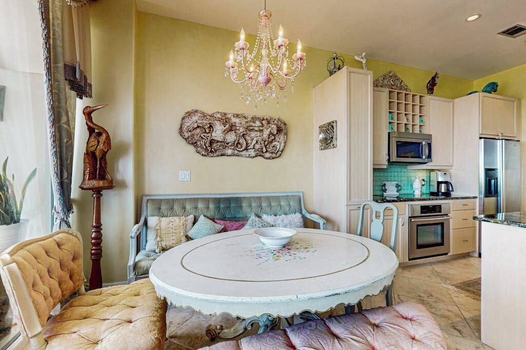A dining area with a round table, chairs, a chandelier, and a sofa.