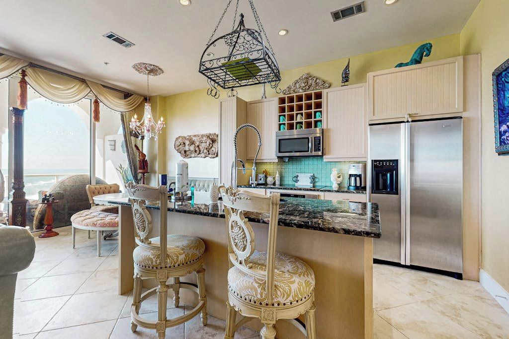 A kitchen with a central island, bar stools, a chandelier, and stainless steel appliances.