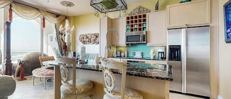 A kitchen with a central island, bar stools, a chandelier, and stainless steel appliances.