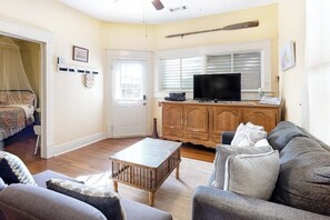 A living room with a sofa, a coffee table, and a television on a wooden cabinet. - Castaway Cottage - Big Backyard & Dog-Friendly (Galveston)