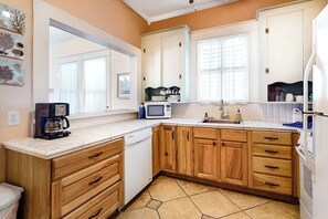 A kitchen with wooden cabinets, a microwave, a coffee maker, and a dishwasher. - Castaway Cottage - Big Backyard & Dog-Friendly (Galveston)