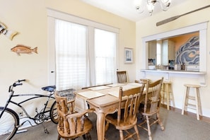 A dining area with a wooden table and chairs, a bicycle, and a large window with blinds. - Castaway Cottage - Big Backyard & Dog-Friendly (Galveston)