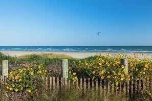 A beach with a wooden fence and sunflowers in the foreground, and the ocean in the background. - Beach to Bay Getaway (Galveston)