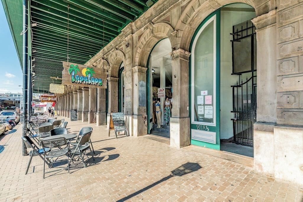 Un bâtiment doté d’un espace extérieur couvert avec des sièges, d’une enseigne représentant des palmiers et d’une façade avec des portes vitrées.
