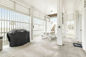 A covered outdoor area with a barbecue grill, a picnic table, and a staircase leading to an upper level. - Seaside Haven - Gulf Views, 2 Blocks to Beach (Galveston)