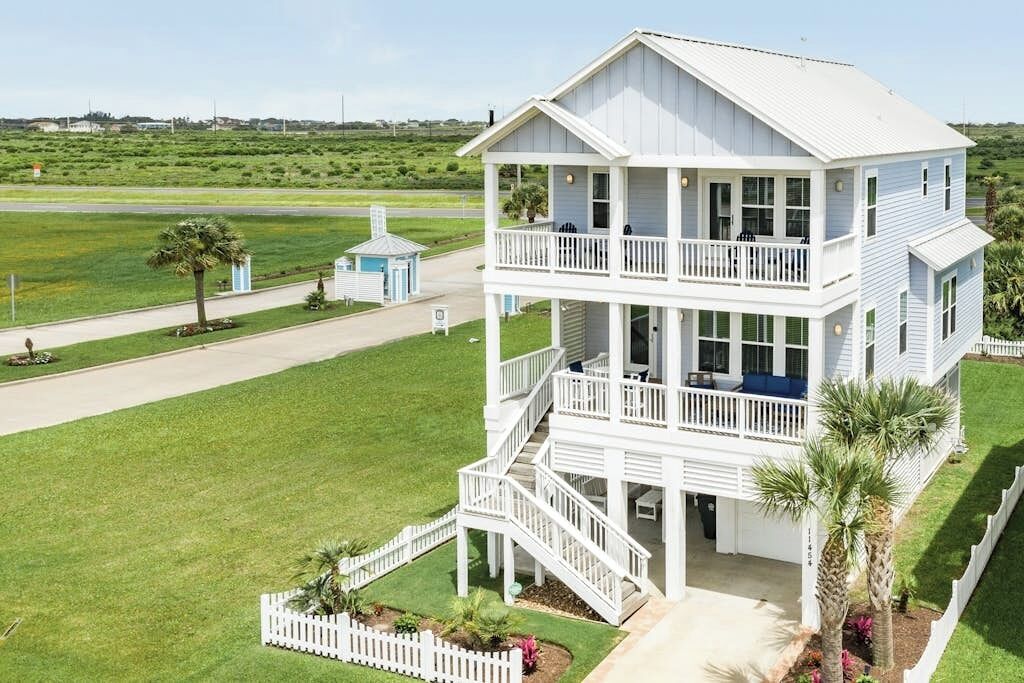 A two-story white building with a balcony on the upper floor, surrounded by a well-maintained lawn and a small structure in the background.