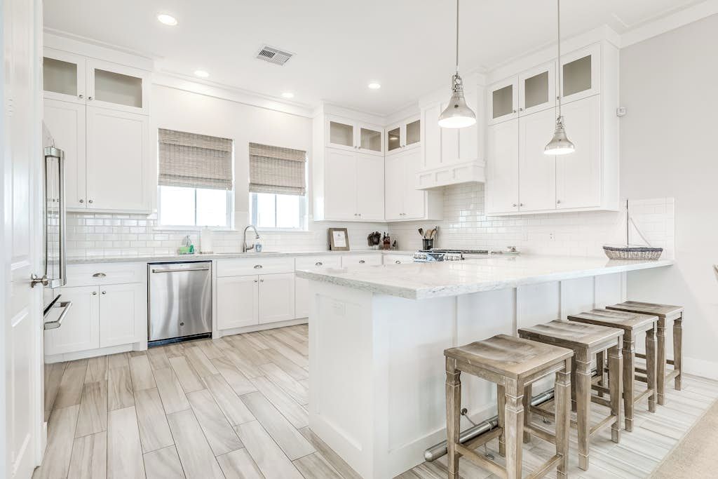 A spacious kitchen with white cabinetry, a large island with bar stools, and a dishwasher.