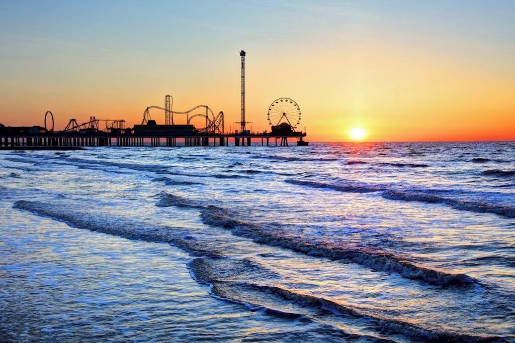 Un molo con giostre e una ruota panoramica al tramonto.